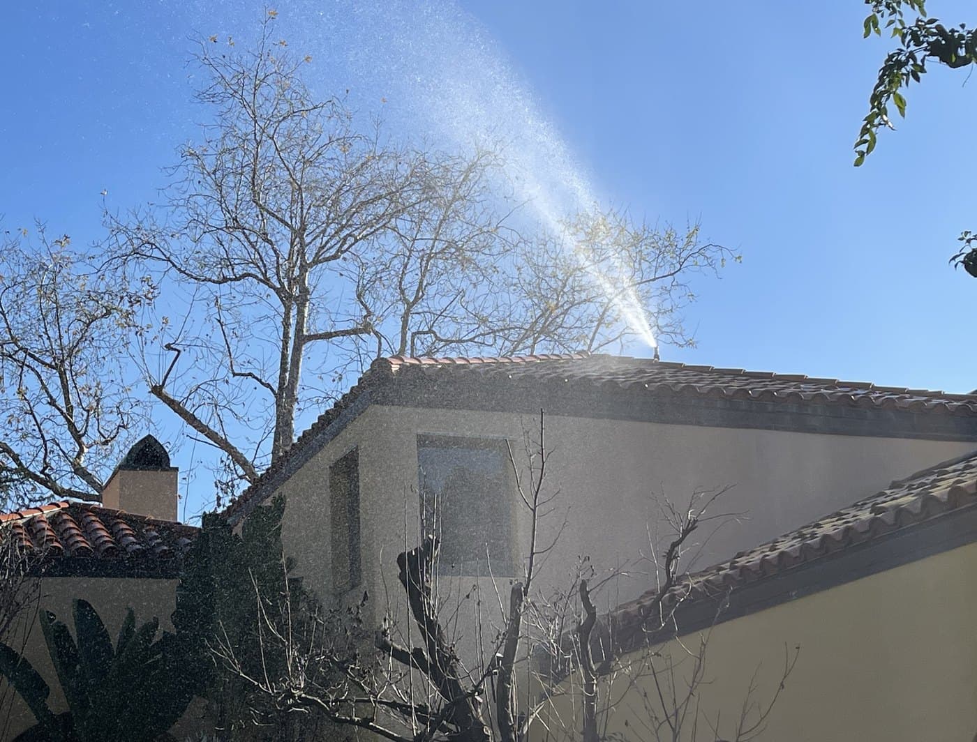 Roof-mounted discharge throwing a wide arc of water across a tile roof and beyond the eaves