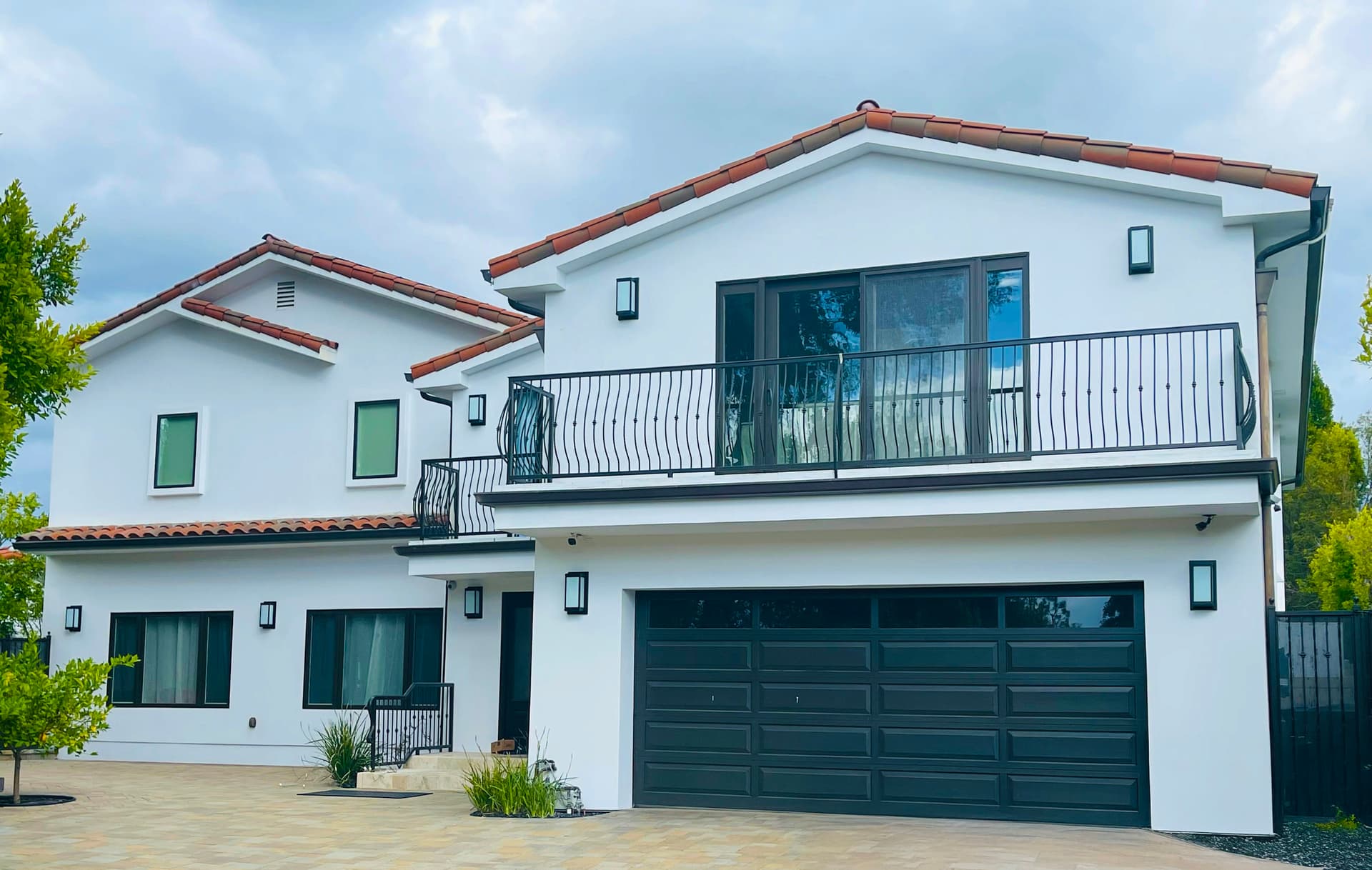 A finished two-story white Spanish-tile home with the FireShield system installed, seen from the driveway — the hardware blended into the roofline and exterior.
